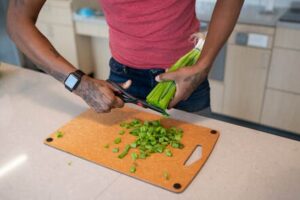 Person snipping the ends of fresh scallions over a cutting board into a pile